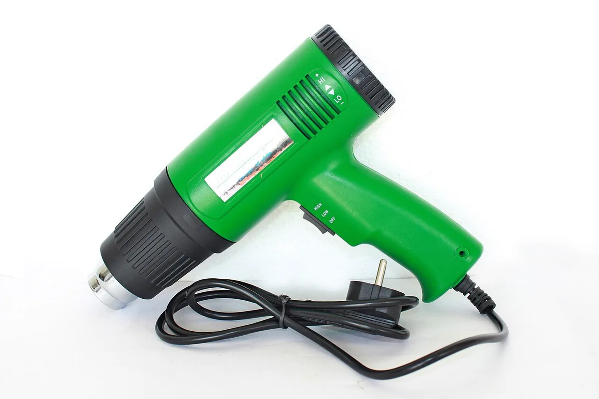 Een groen heteluchtpistool met zwart mondstuk en snoer, op een witte ondergrond.