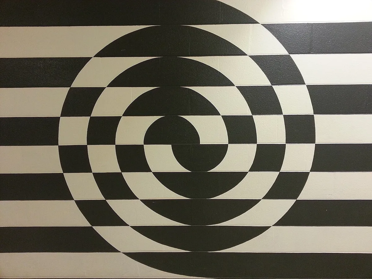 Muurschildering met een zwart-wit patroon van concentrische cirkels en horizontale strepen over een hele wand.