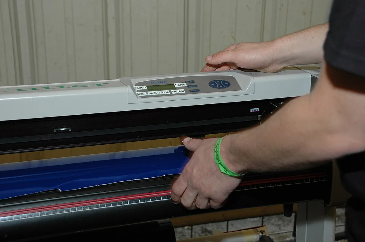 Iemand voert een baan blauwe vinylfolie in een snijplotter.